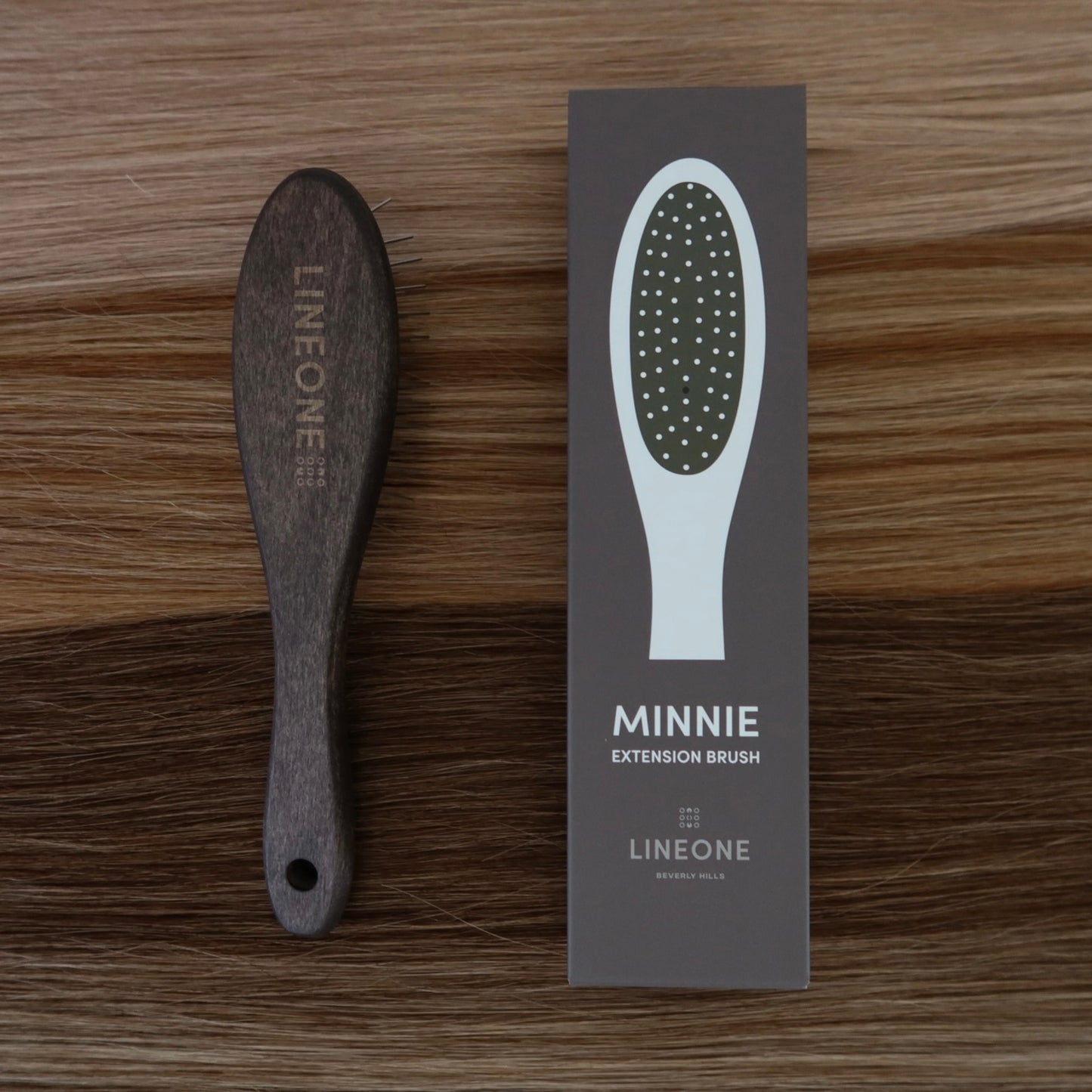 LINEONE Hair MINNIE Extension Brush with dark wood handle next to its packaging box on blonde hair