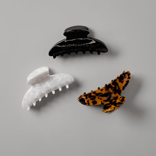 Three LINEONE Hair Claw Clips in glossy Black, Tortoise and White Pearl arranged on grey background
