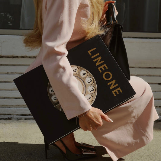 Stylist in pink suit holding LINEONE Hair Bookcase volume with gold rotary-dial cover on steps
