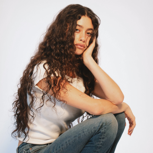 LINEONE Hair Genius Weft Wavy on model with long voluminous curly brunette extensions and white tank top
