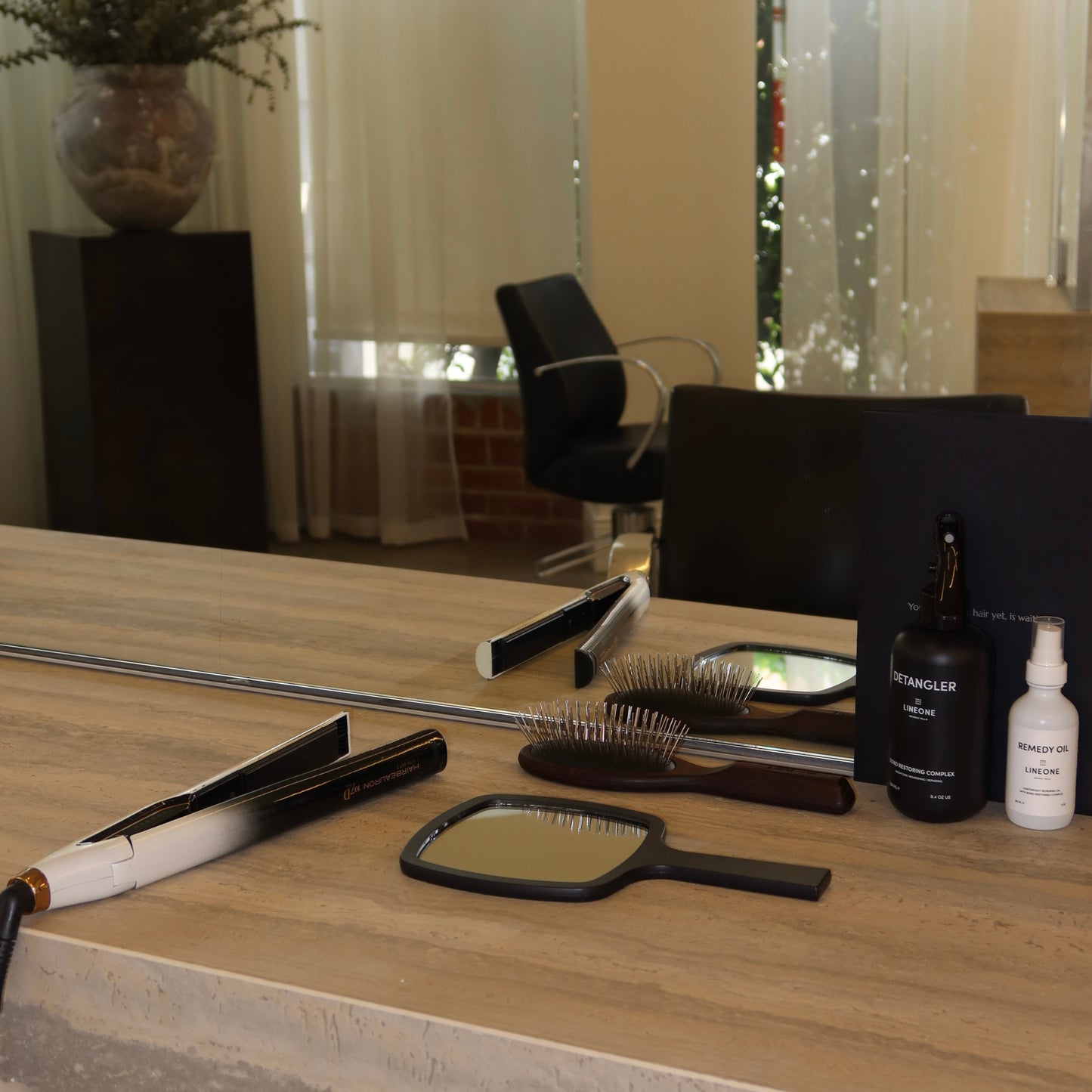 Salon station with flat iron, paddle brush, Remedy Oil, Detangler and the LINEONE Hair Mirror laid on wood