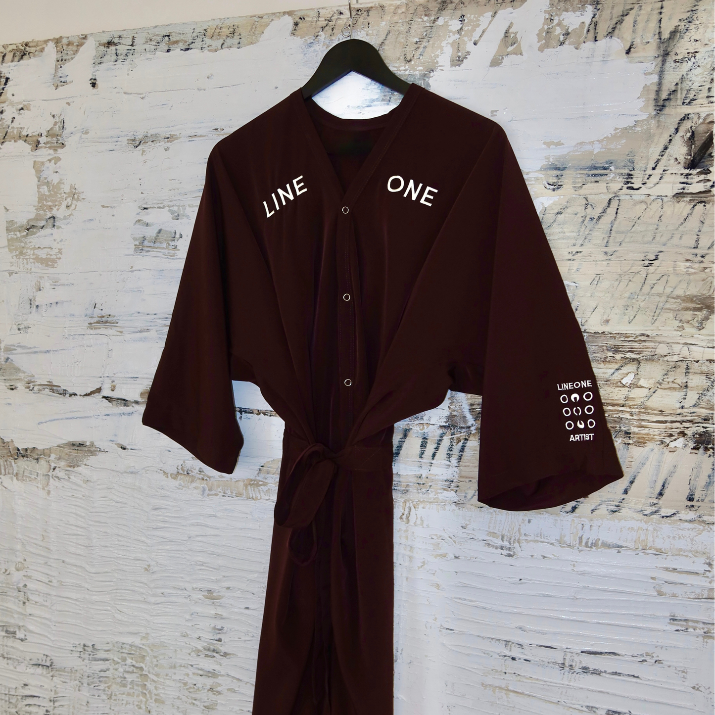 Single Coco-color LINEONE Hair Client Robe tied at waist hung on rustic painted board