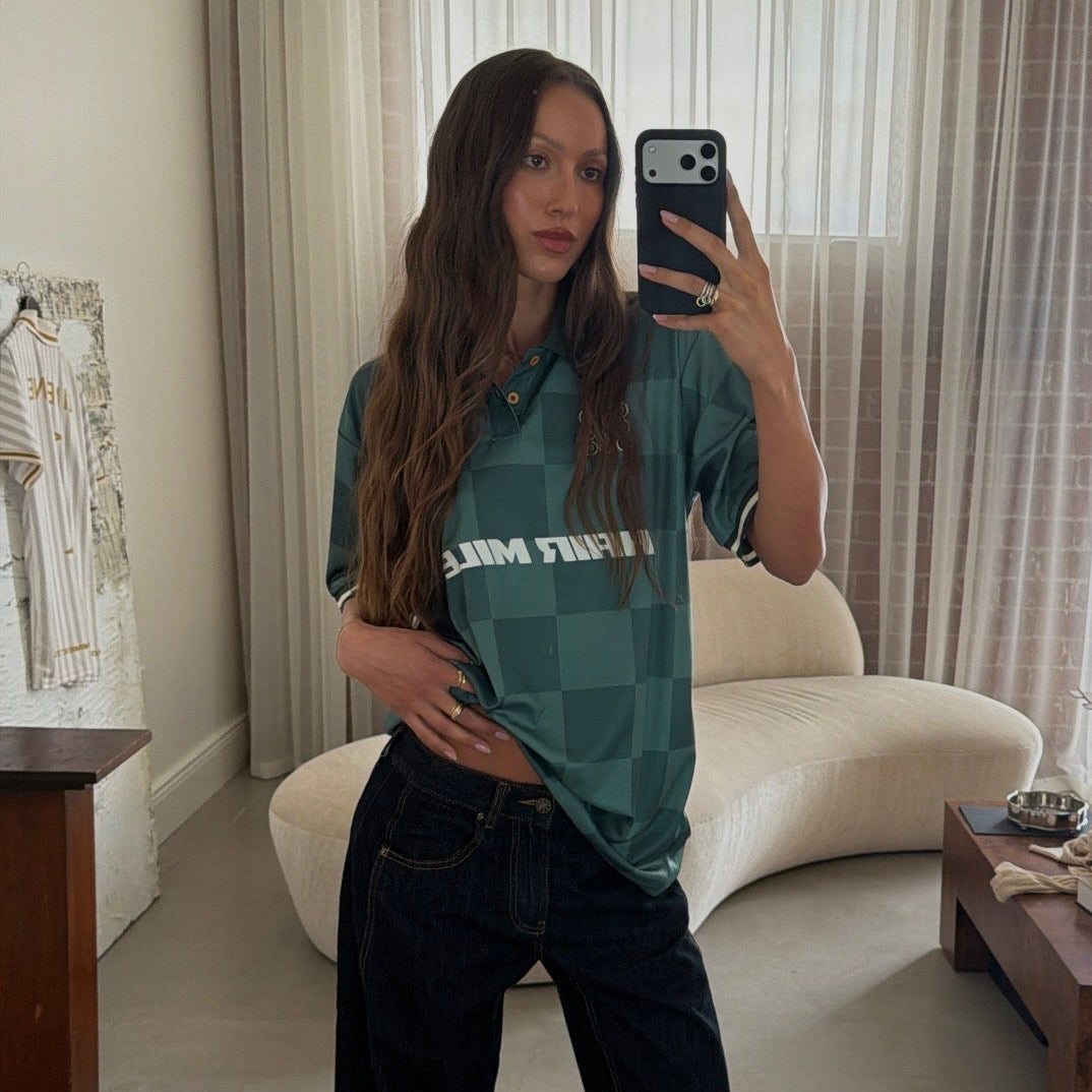 Mirror selfie of brunette model wearing LINEONE Hair Team Works Jersey in green Hair Miles home kit