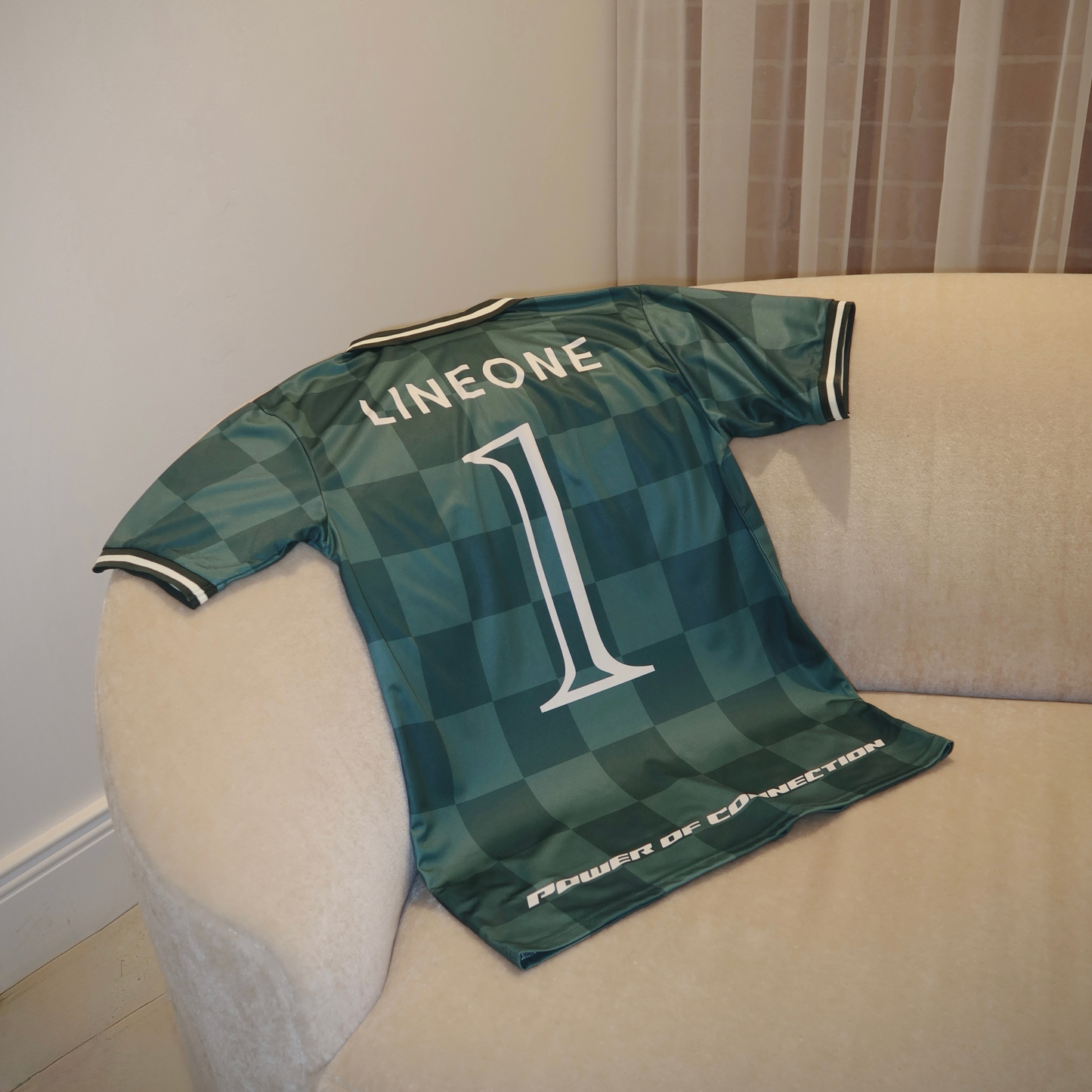 LINEONE Hair Team Works Jersey green home kit draped on cream sofa showing back LINEONE number 1