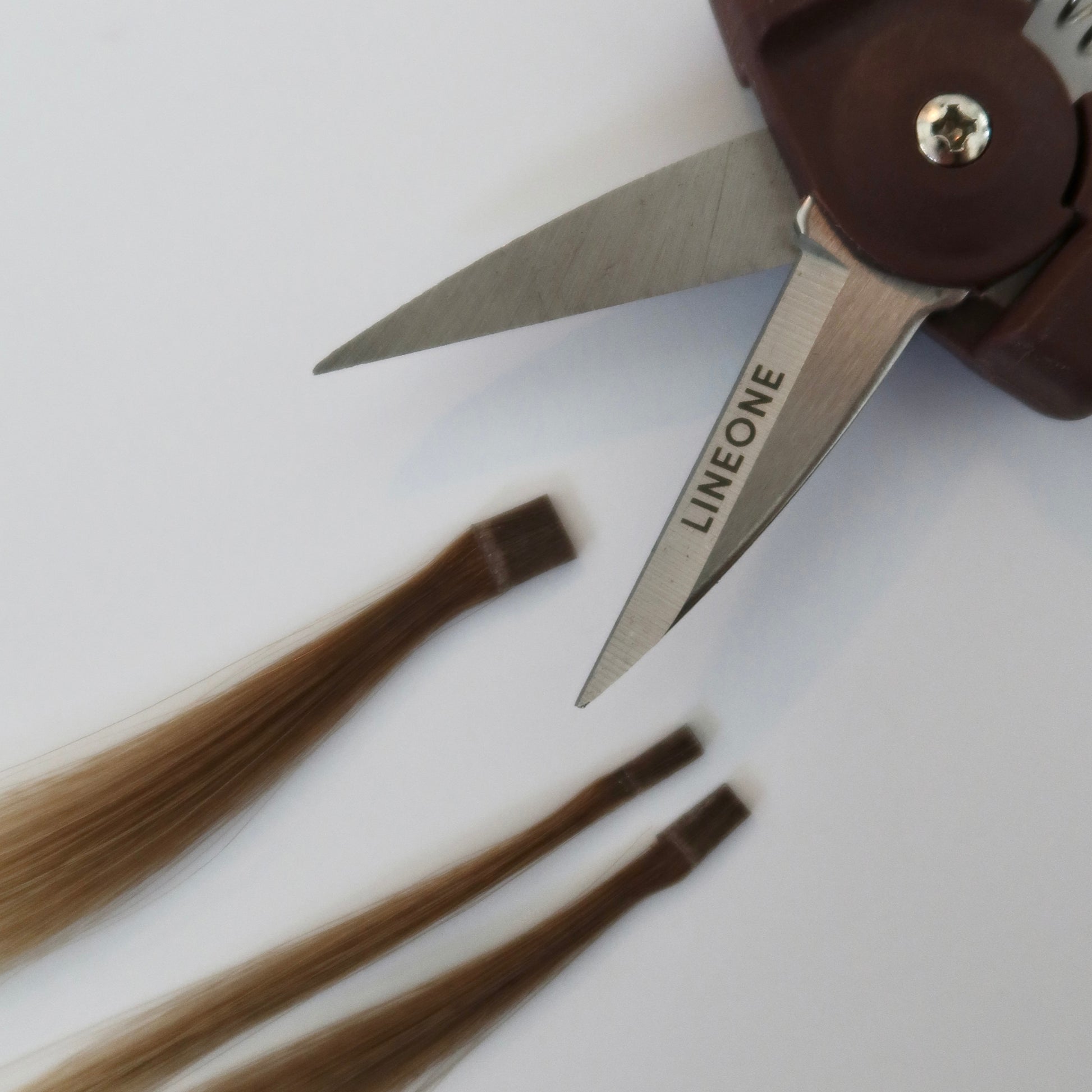 Close-up of LINEONE Bond mini trimmer blade with hair weft strands showing precision cutting capability on white background