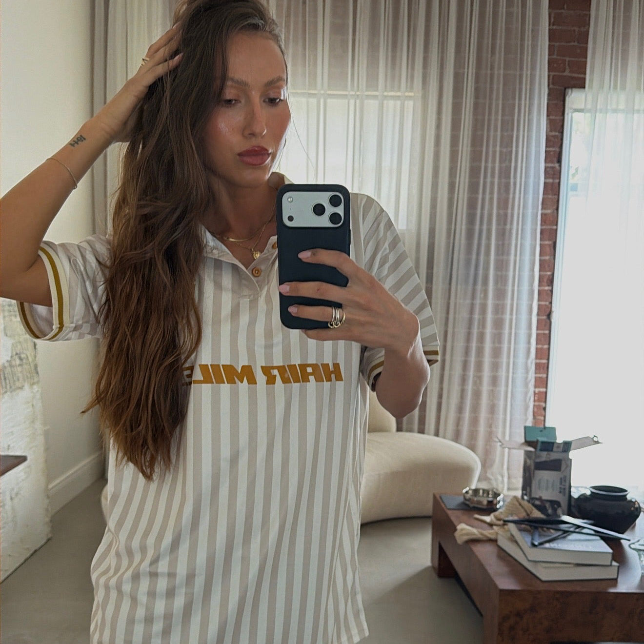 Mirror selfie of model in LINEONE Hair Team Works Jersey cream away kit with gold stripes and Hair Miles print