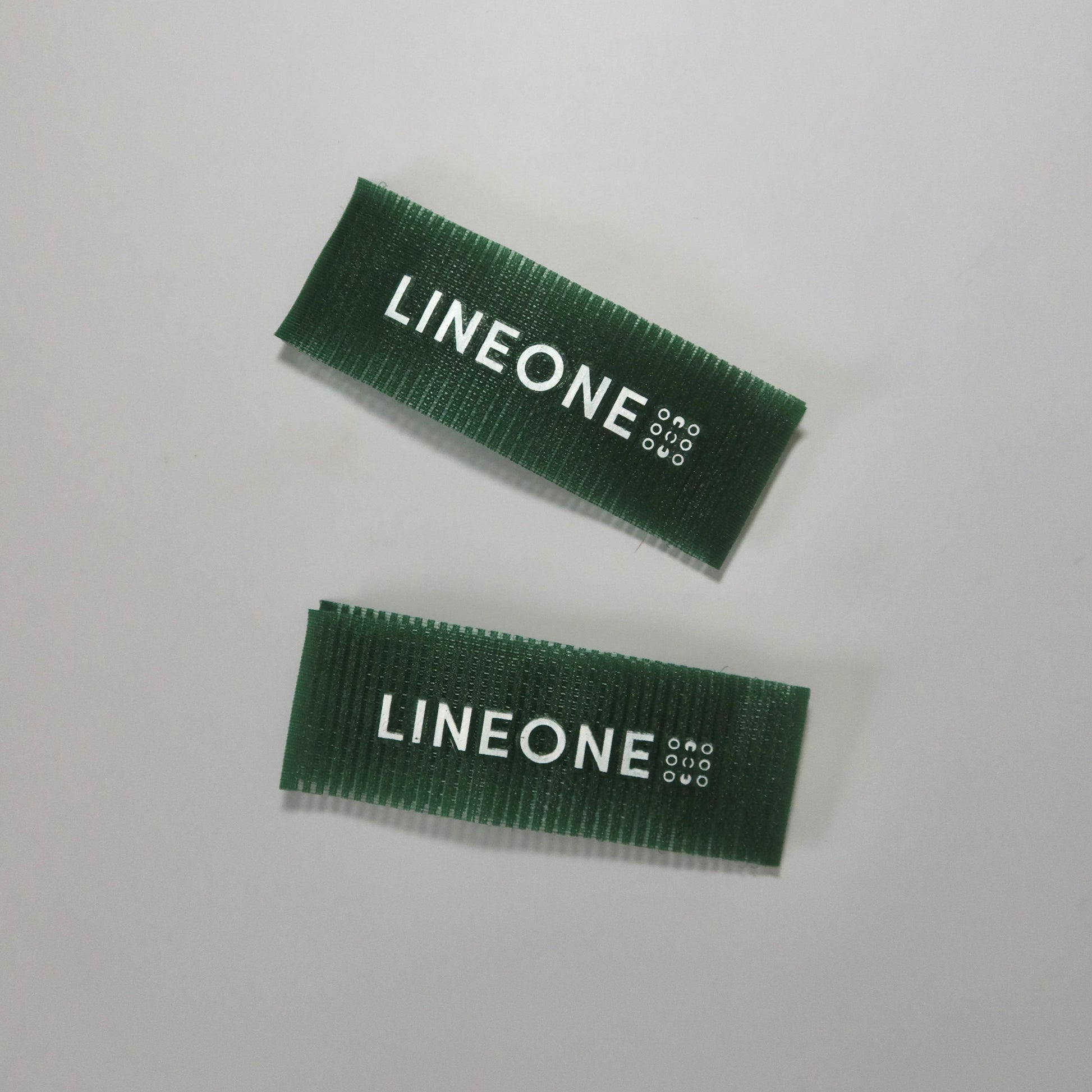 Pair of LINEONE Hair Grippers in hunter green velcro arranged diagonally on grey surface