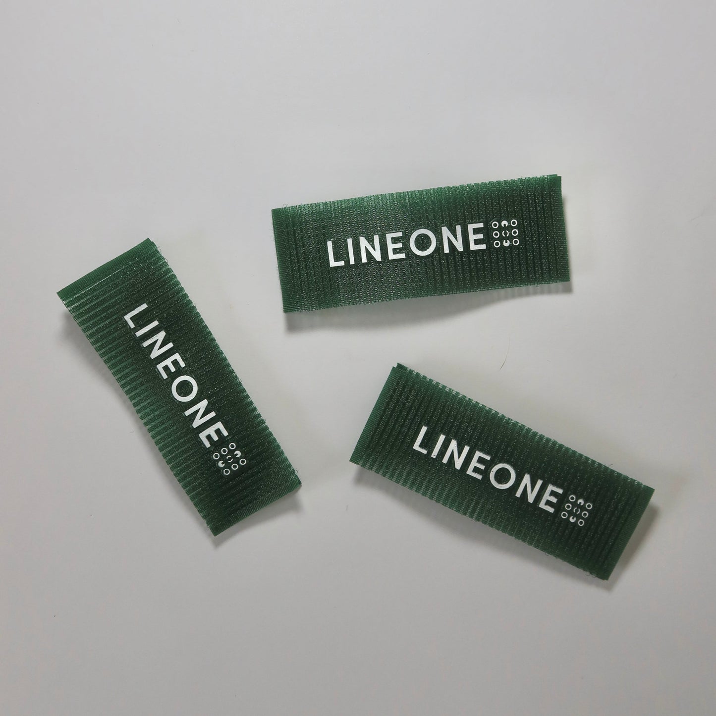 Three LINEONE Hair Grippers in hunter green velcro strips with white logo on white background