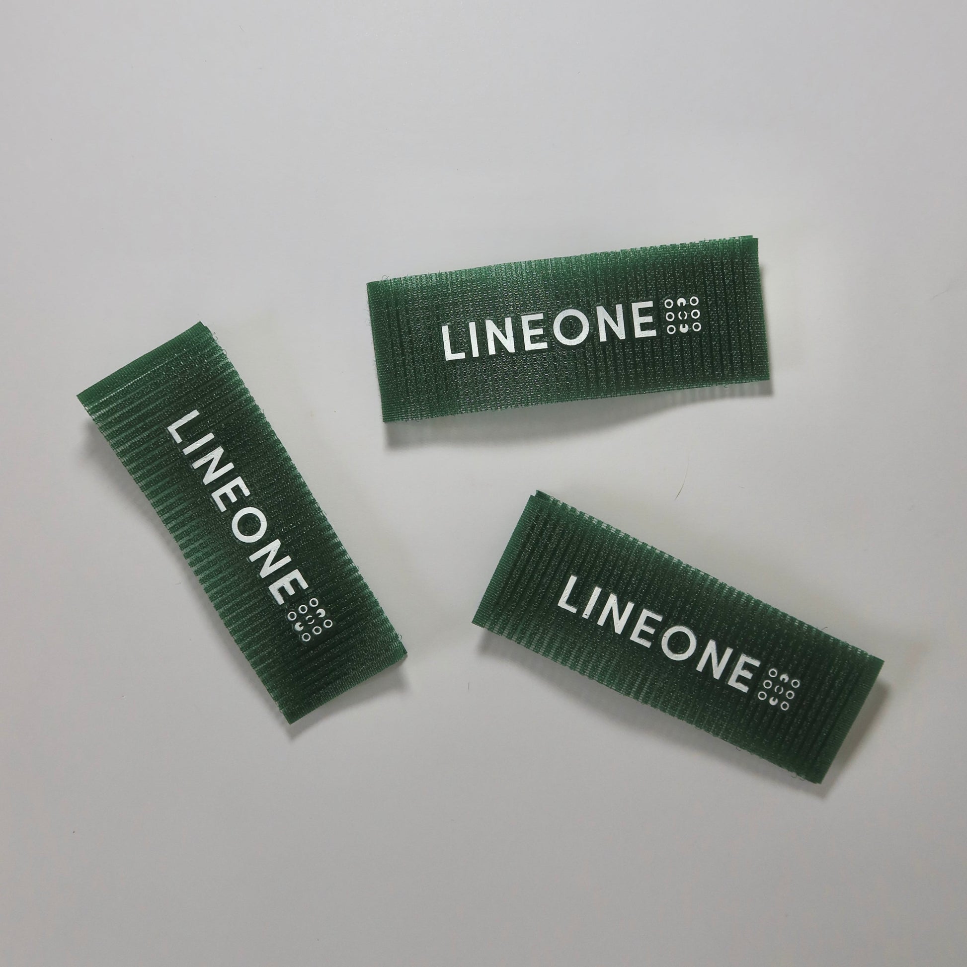 Three LINEONE Hair Grippers in hunter green velcro strips with white logo on white background