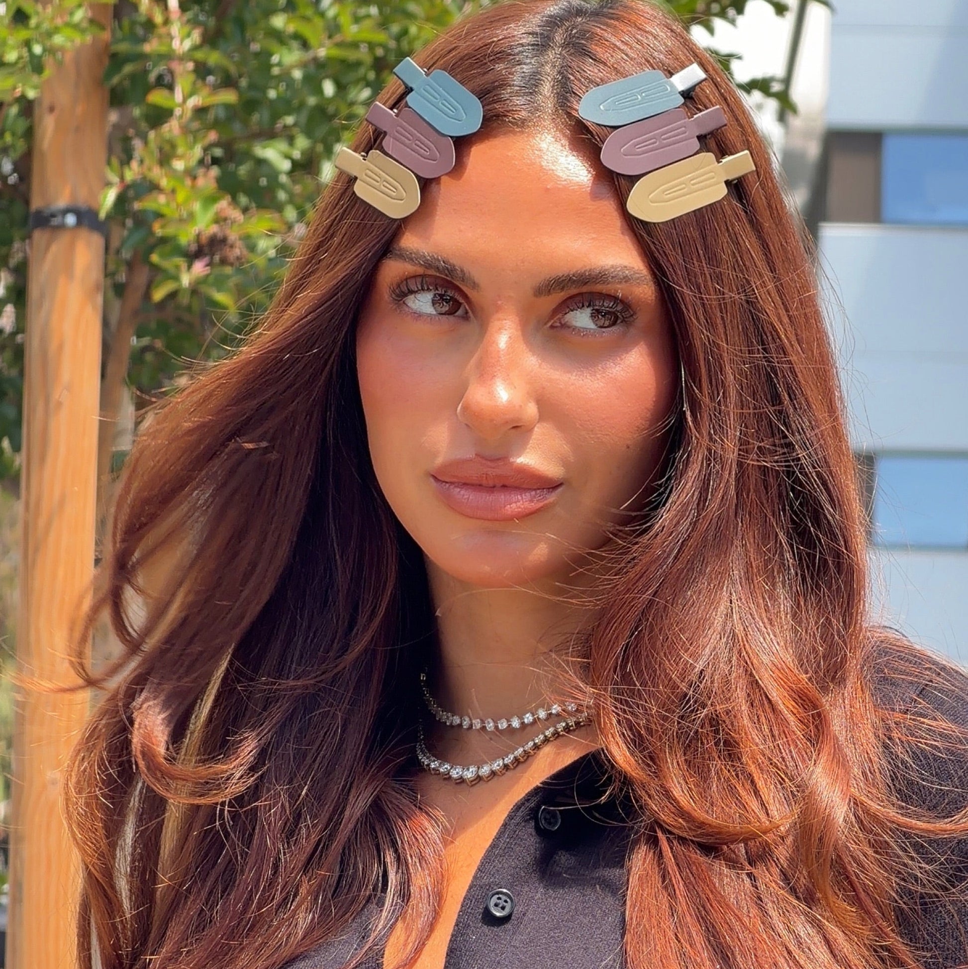 Brunette model outdoors wearing four LINEONE Hair Please Hold Clips in slate, plum, sand and olive at her hairline
