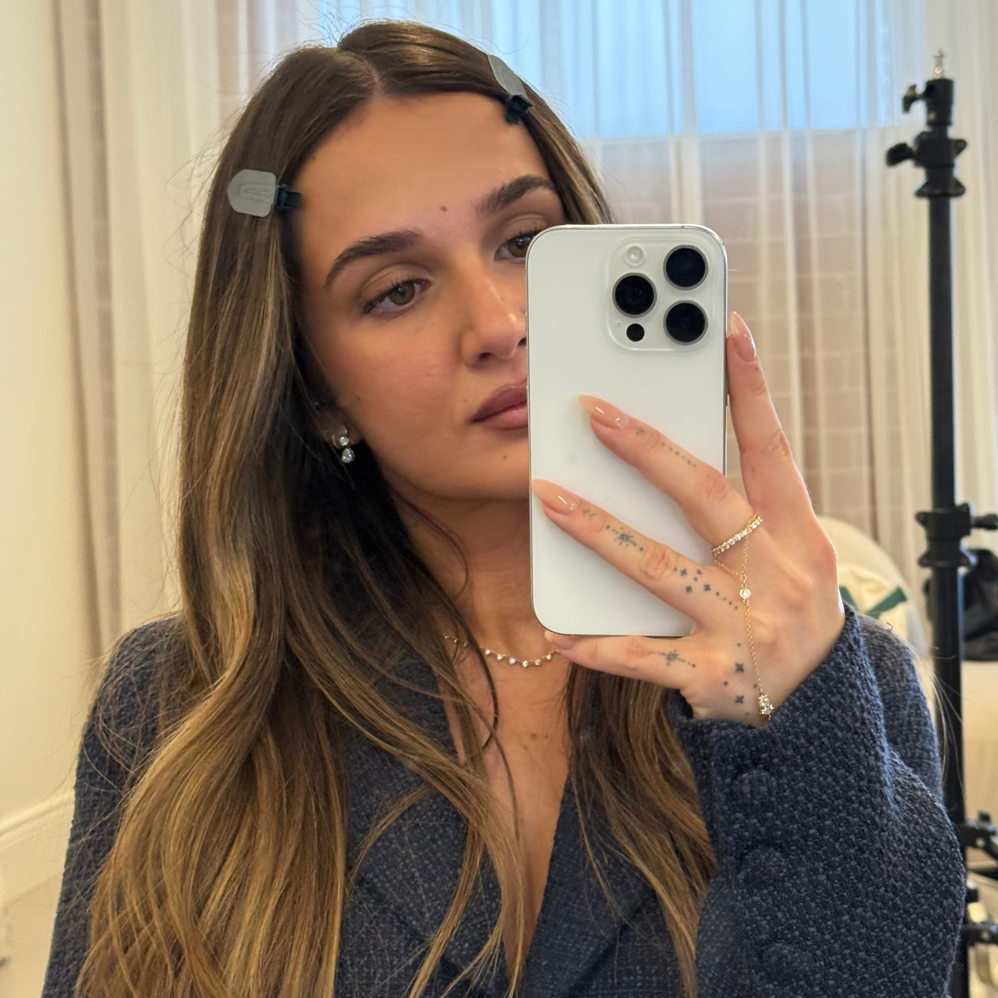 Mirror selfie of a woman in navy cardigan wearing two olive LINEONE Hair Please Hold Clips at her crown