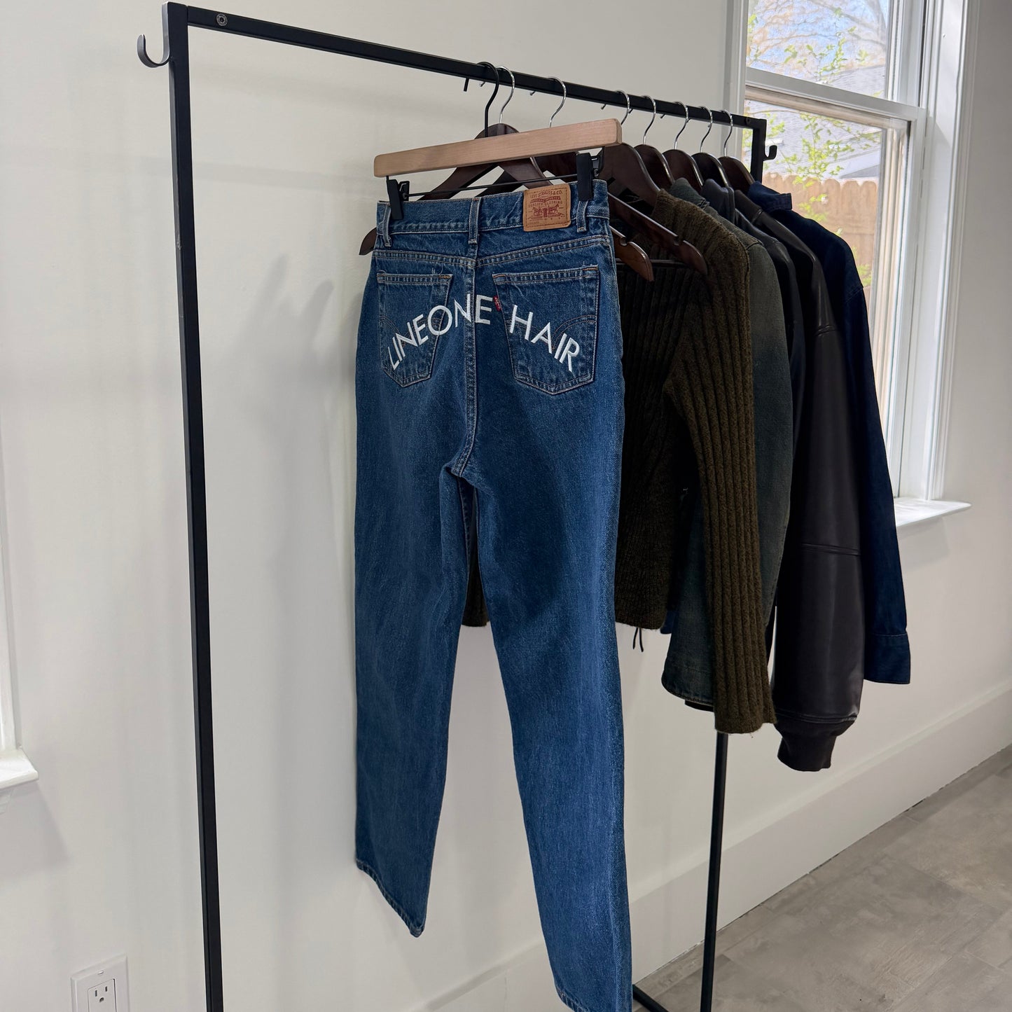 LINEONE Hair Jeans hung on garment rack alongside knits and leather, embroidered back pockets visible