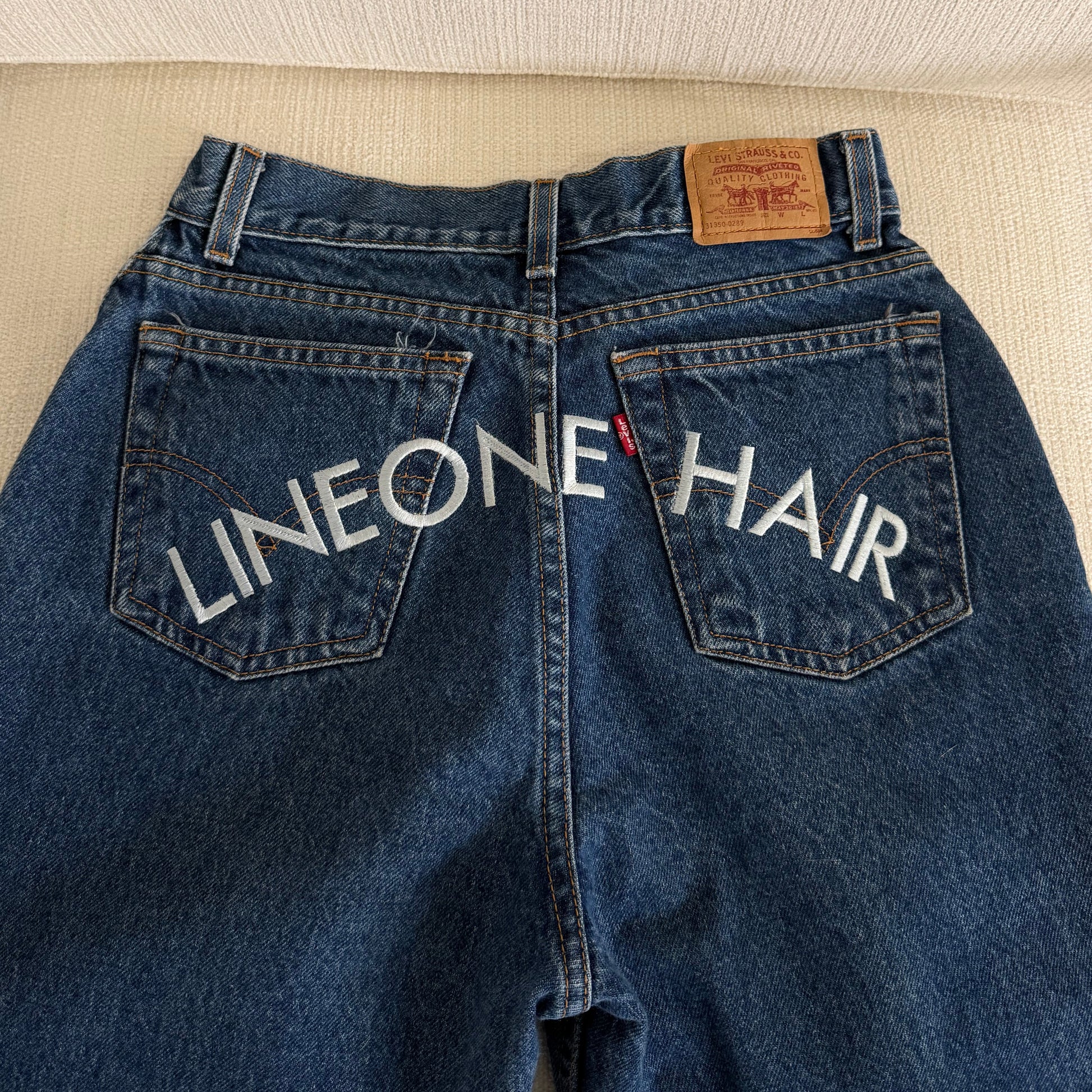 LINEONE Hair Jeans close-up of dark indigo back pockets with white LINEONE Hair arched embroidery