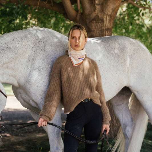 Blonde rider in camel knit and silk scarf holding reins beside a grey horse, LINEONE Hair Weft Intro Kit Dimensional Blonde