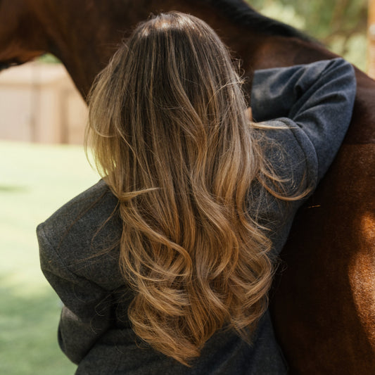 Back view of long dimensional brunette waves on a rider in grey wool beside a chestnut horse, LINEONE Hair Hybrid Intro Kit