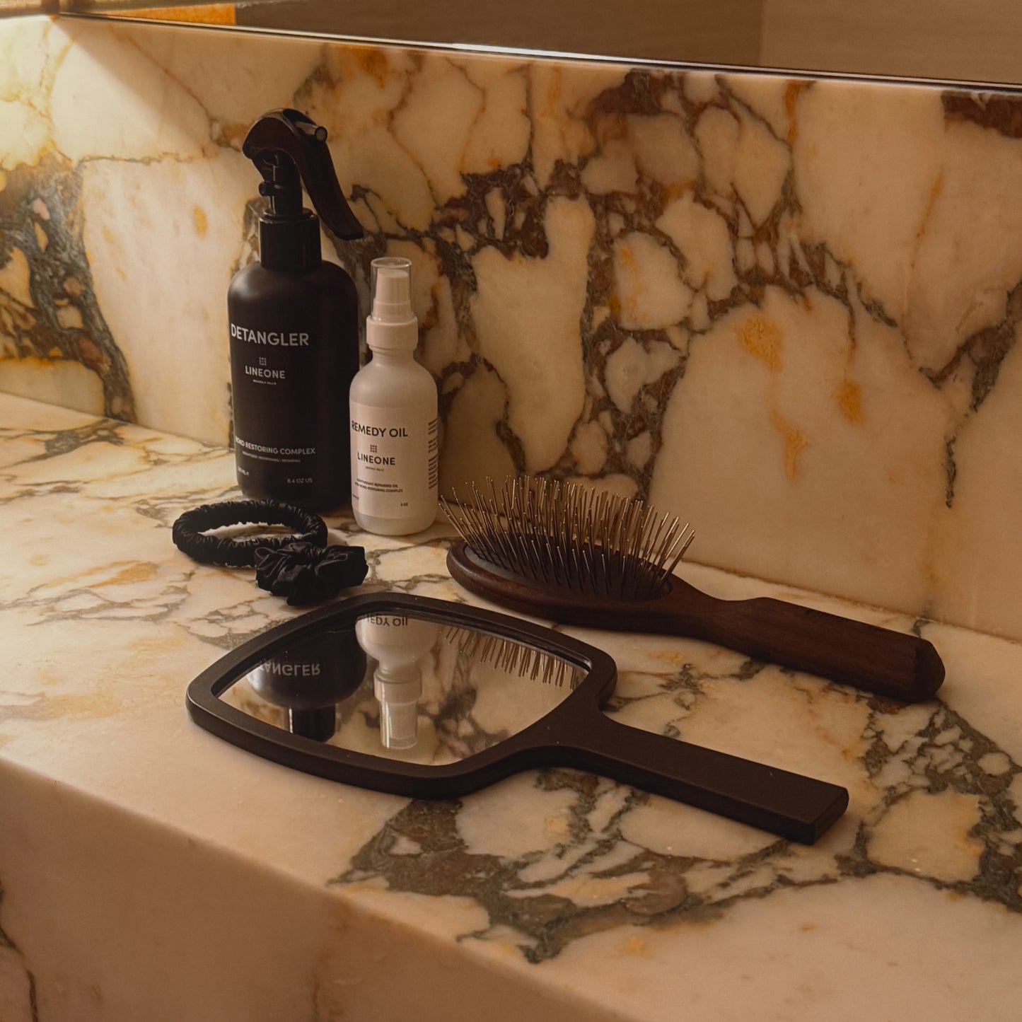 LINEONE Hair Mirror laid face up on marble reflecting Detangler and Remedy Oil bottles with paddle brush nearby