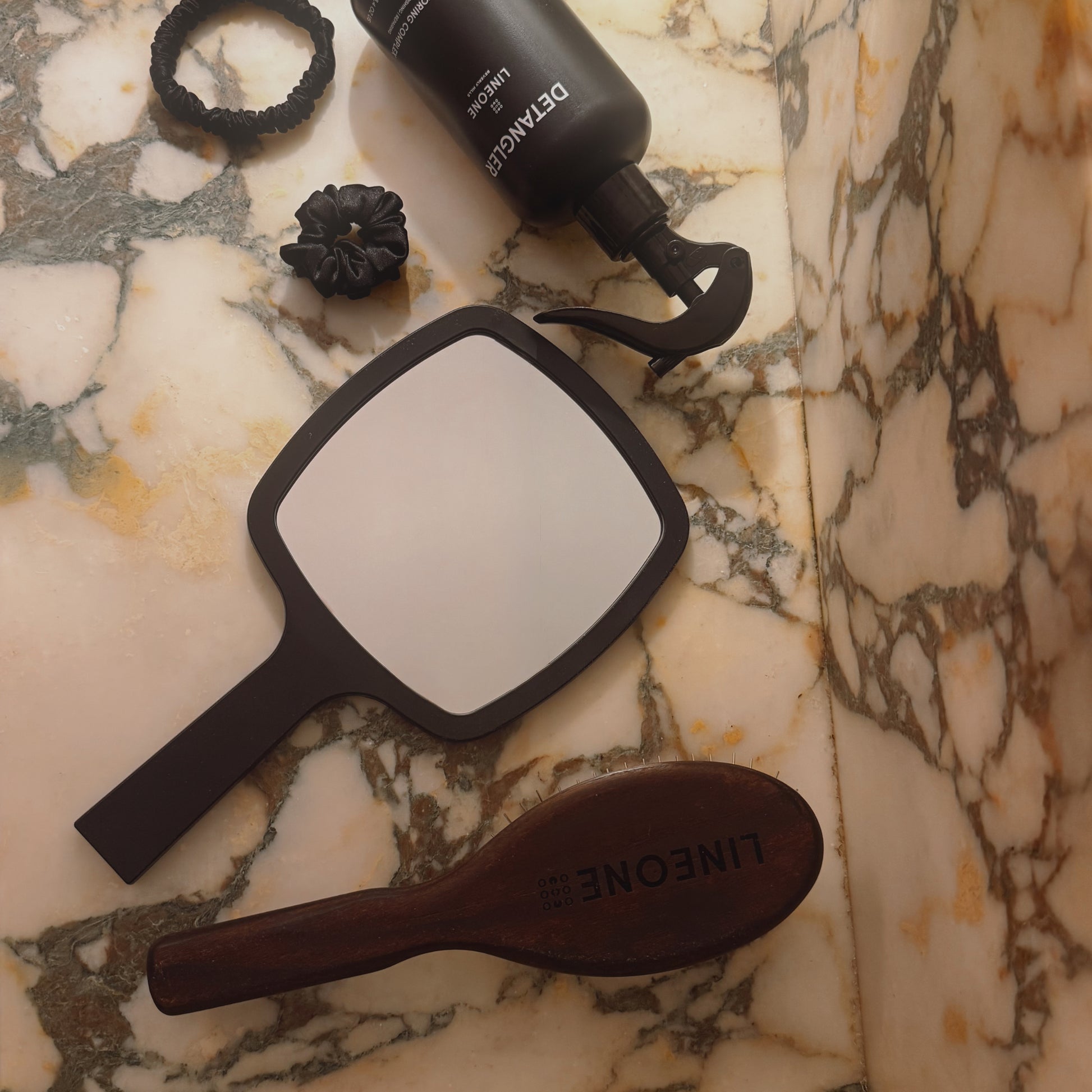 Overhead of LINEONE Hair Mirror on marble counter with Detangler bottle, wooden brush and silk scrunchies