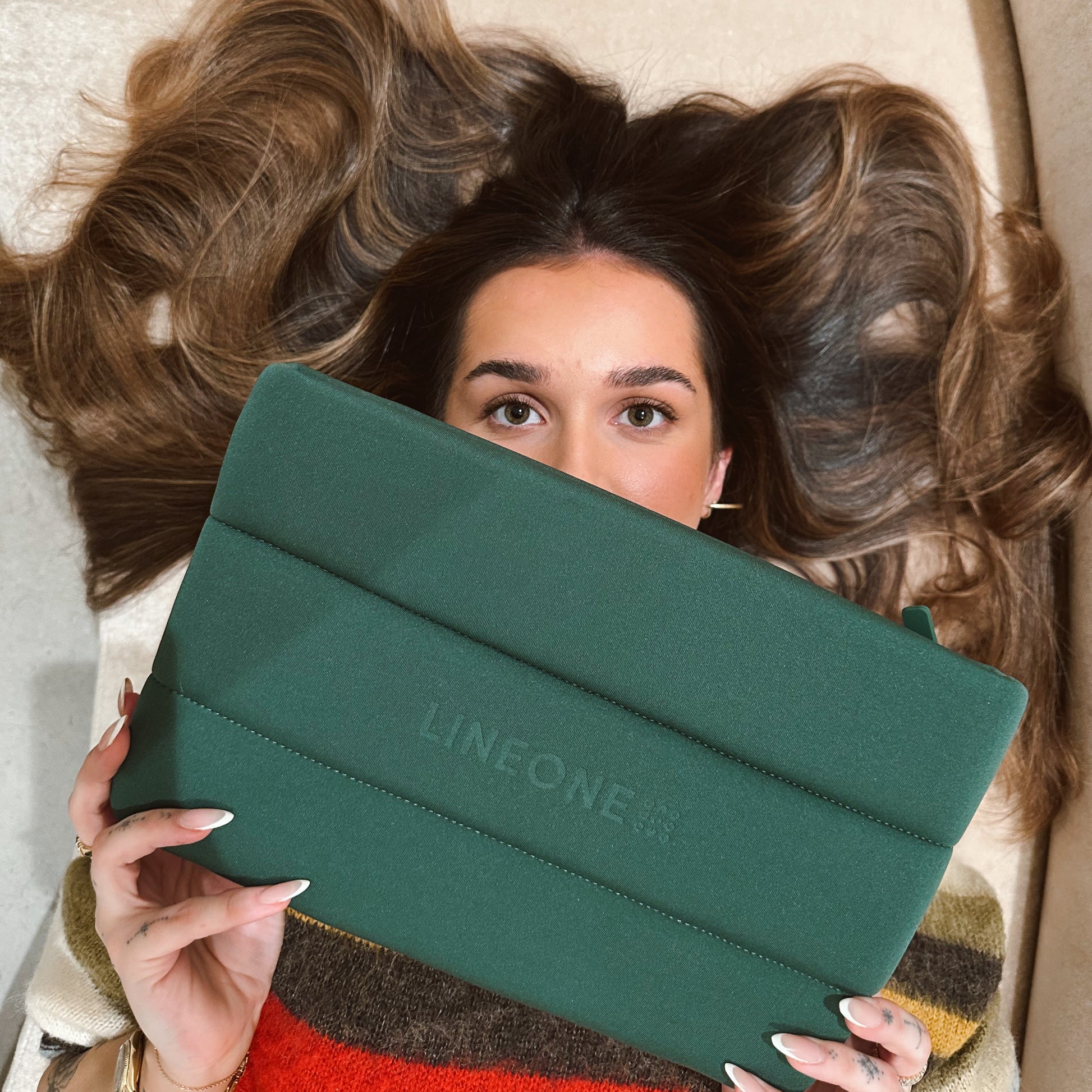 Model with bouncy wavy brunette hair holding LINEONE Hair The Carry On hunter green pouch to face