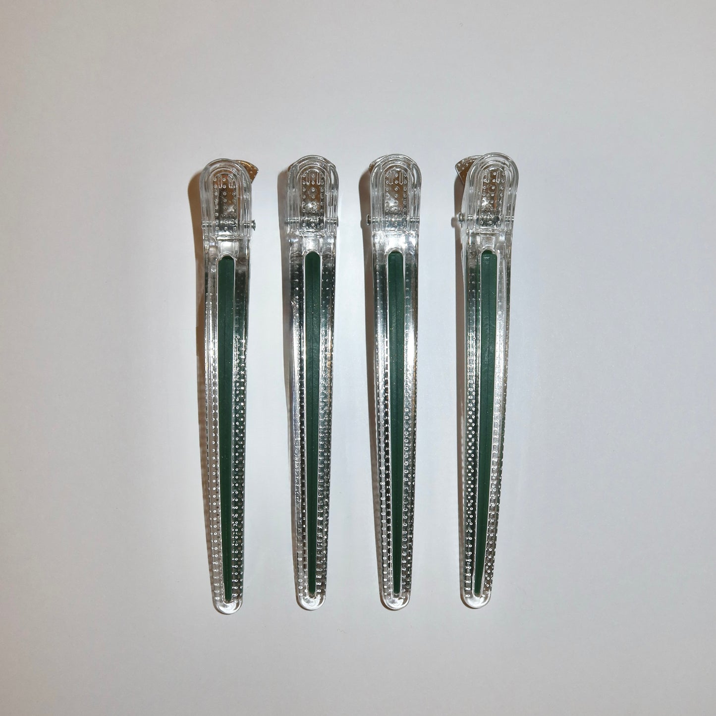 Four LINEONE Hair Creaseless Sectioning Clips in clear bodies with hunter green strip inserts lined up