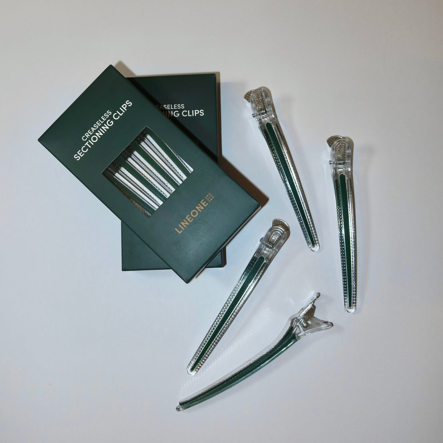 LINEONE Hair Creaseless Sectioning Clips flat lay with two stacked green boxes and scattered clips