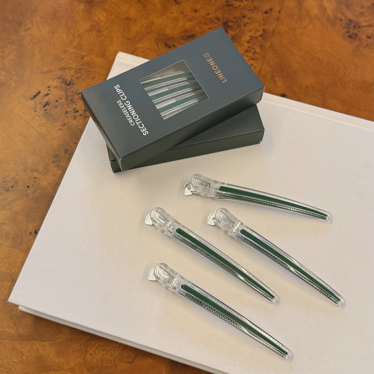 LINEONE Hair Creaseless Sectioning Clips lifestyle with green box stack on book over burl wood desk