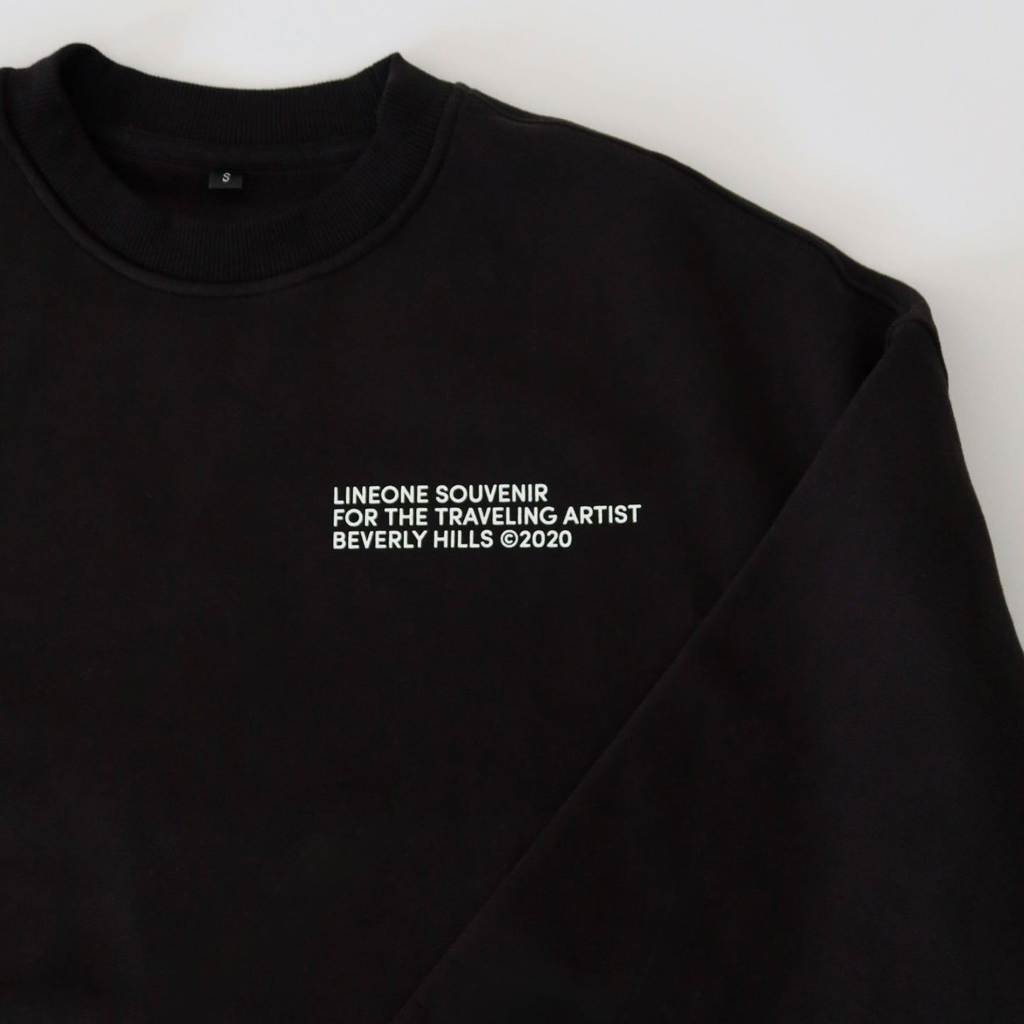 Close-up of black LINEONE Hair Pantone Crewneck collar and white LINEONE Souvenir Beverly Hills chest print