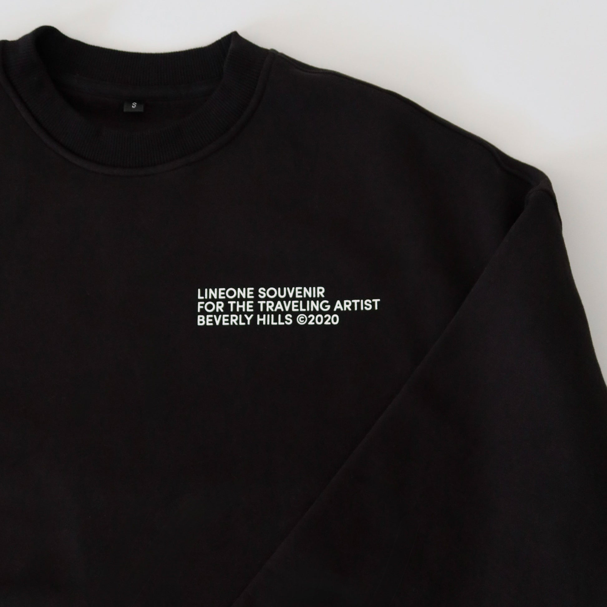 Close-up of black LINEONE Hair Pantone Crewneck collar and white LINEONE Souvenir Beverly Hills chest print