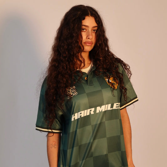 Person wearing a green checkered shirt with 'HAIR MILES' text on a plain background