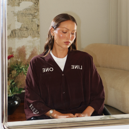 Model in mirror wearing Coco-color LINEONE Hair Client Robe with cream tee underneath