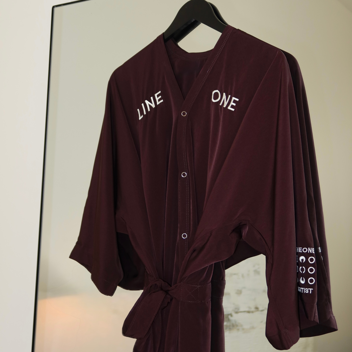 Coco-color LINEONE Hair Client Robe on wooden hanger hung against mirror with copper LINEONE shoulder text
