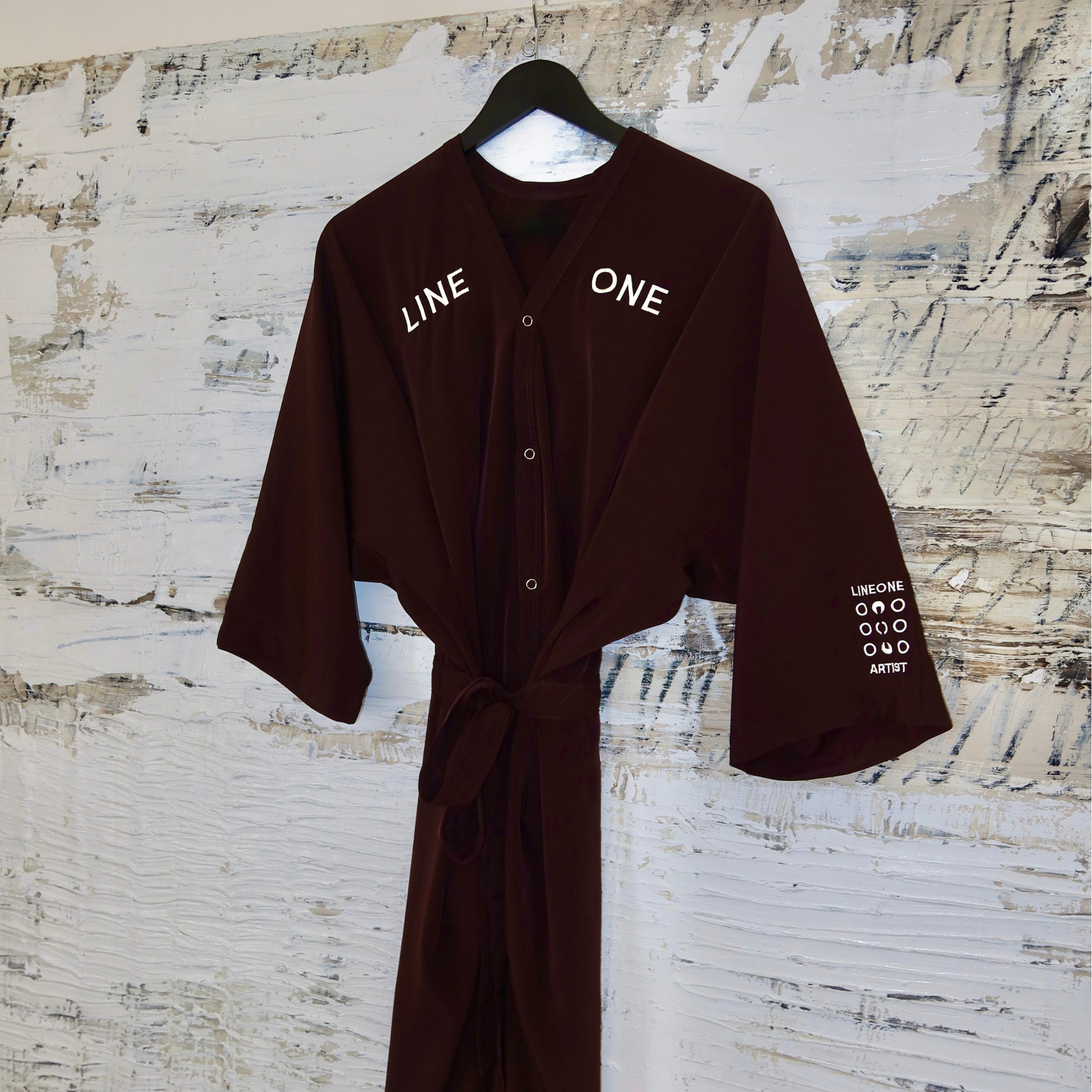 Single Coco-color LINEONE Hair Client Robe tied at waist hung on rustic painted board
