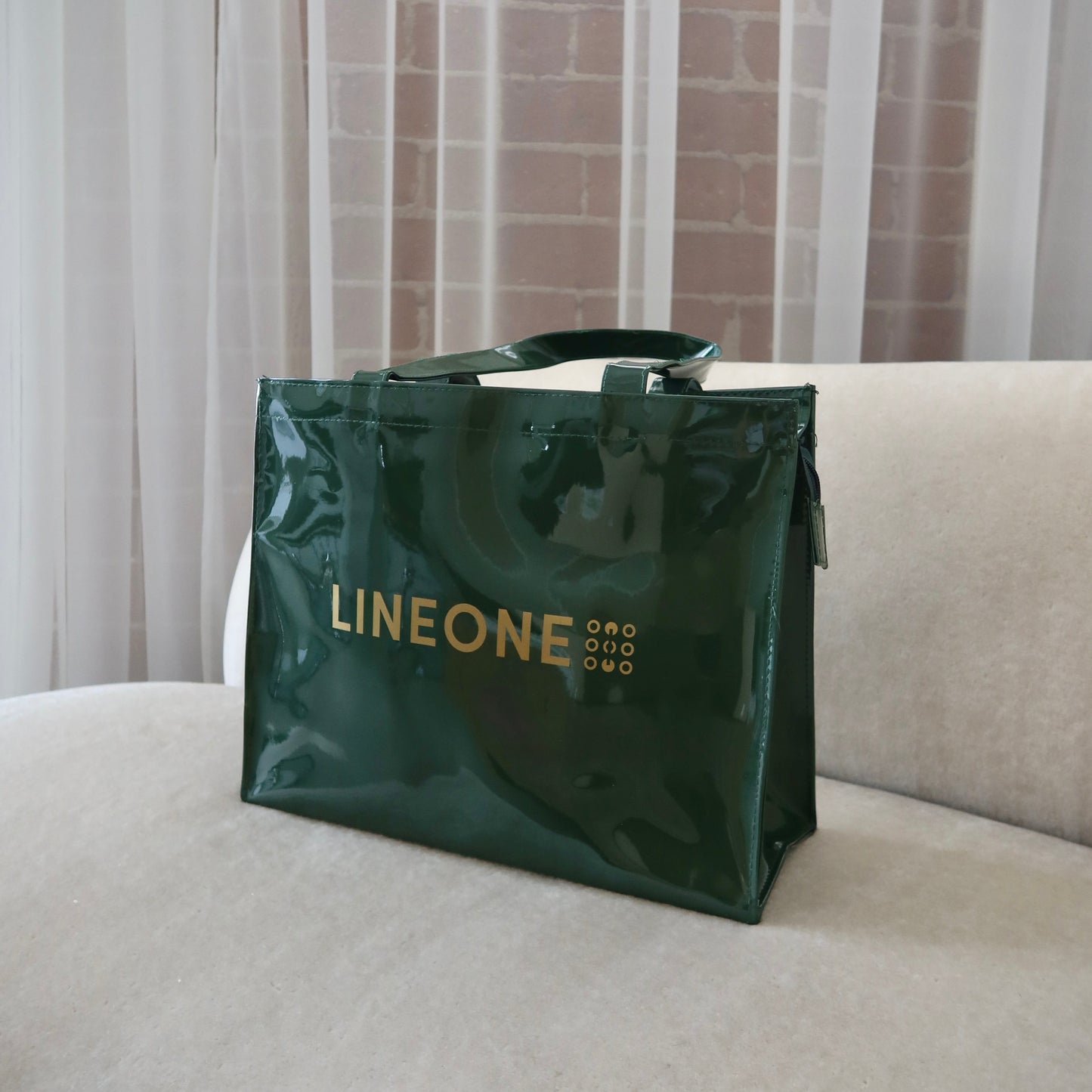 Hunter green patent LINEONE Hair Rodeo Bag with gold logo on a cream sofa with linen curtains