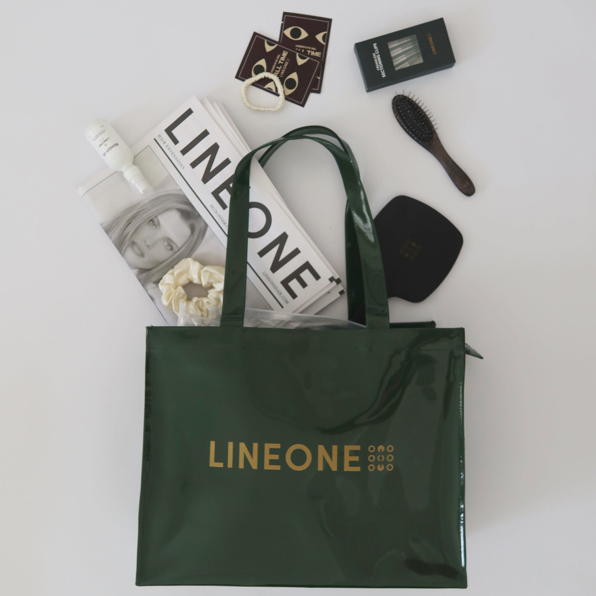 Flat lay of LINEONE Hair Rodeo Bag in hunter green with newsprint, brush, Mirror, scrunchie and clip pack